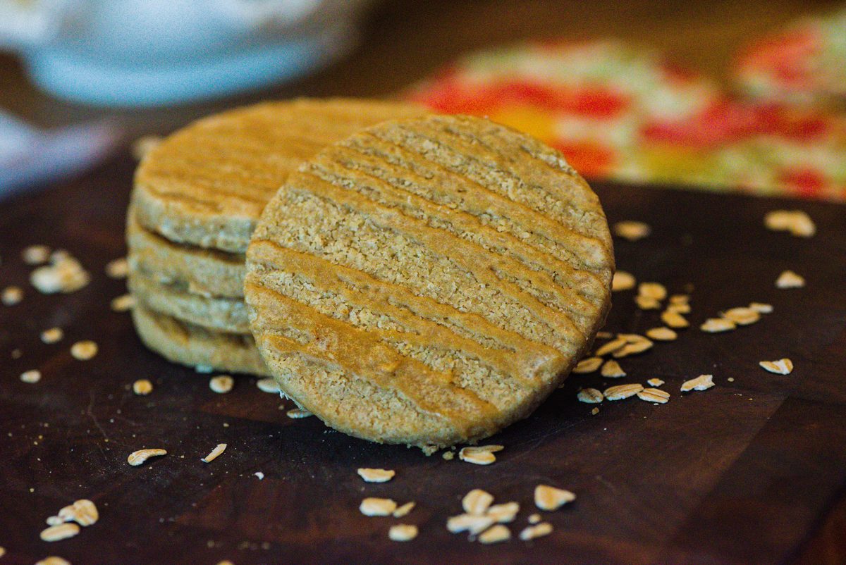 A stack of maple oat shortbread on a dark wooden board, scattered with oats