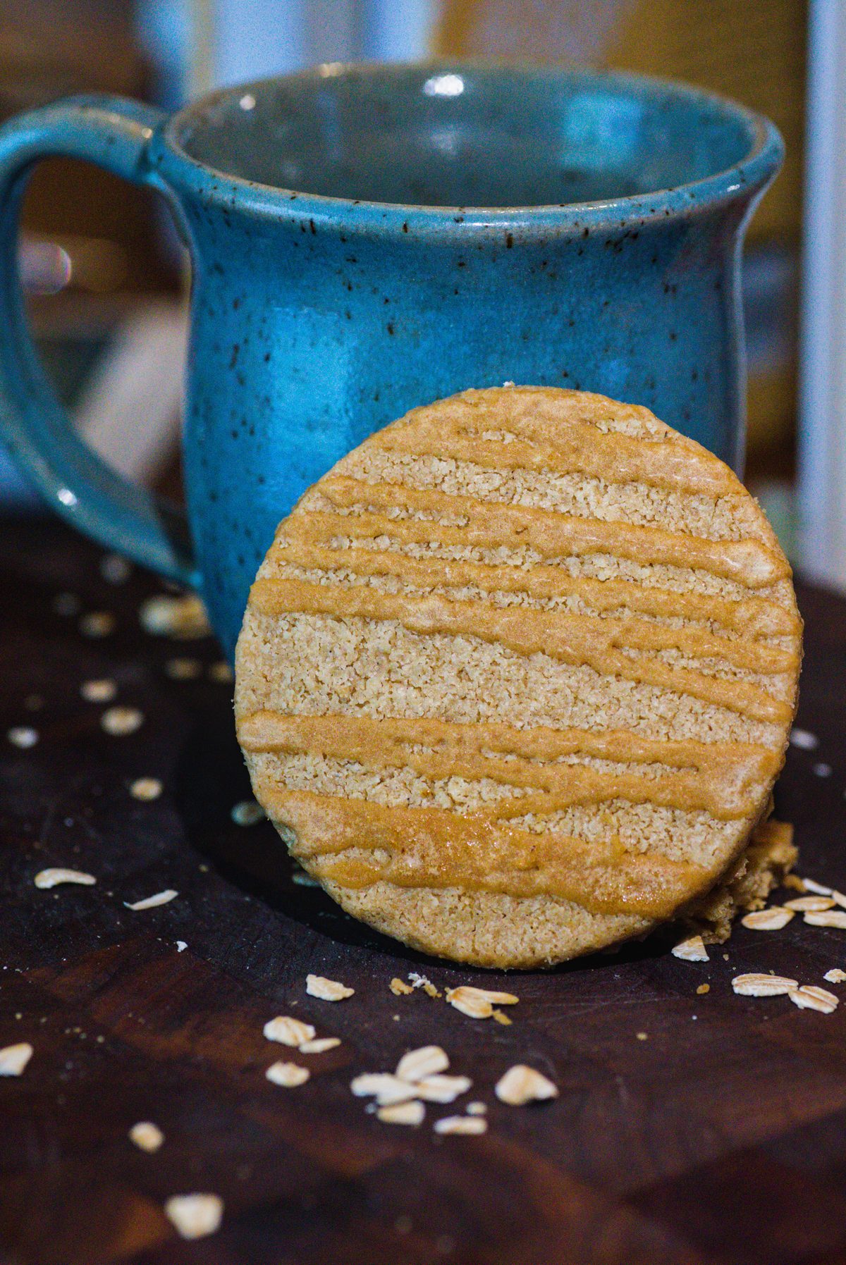 A maple oat shortbread round leaning against a blue speckled mug